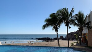 Área de piscina com espreguiçadeiras, vista para a praia e palmeiras.