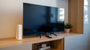 Un televisor de pantalla plana sujeto a un estante de madera, con un control remoto y un altavoz blanco a su lado.