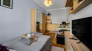 Un espacio habitable compacto con cama, escritorio, televisor y kitchenette.