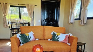 A living room with a sofa, two side tables, a patterned rug, and a view of greenery outside. - Charming fully equipped cottage in Valle de Guadalupe - Early check in! (Ensenada)