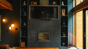 A cozy living room with a wooden coffee table, leather sofas, a fireplace, and built-in shelving with various decorative items.