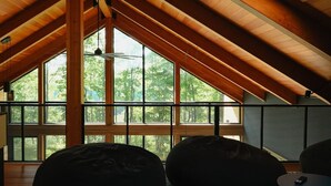 A spacious attic room with wooden beams, large windows, and a patterned rug.