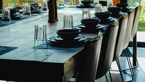 A dining table set with chairs, large windows, and a view of trees.