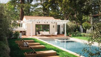 Relax in a serene backyard with a swimming pool, lush greenery, and comfortable seating options.