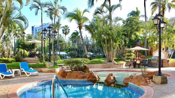 Un espace piscine doté de chaises longues, d’un jacuzzi et de palmiers.