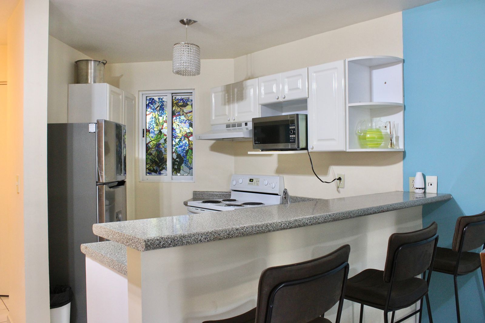 A compact kitchen with a refrigerator, microwave, stove, and bar stools.