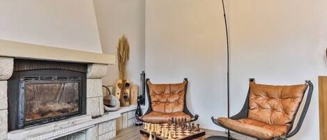 Un salón con chimenea, dos sillones de cuero, una mesa de centro y un tablero de ajedrez.