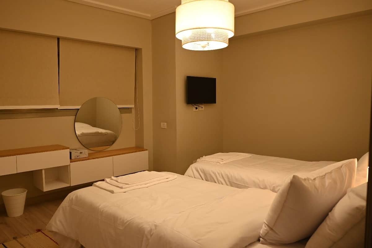 A hotel room with two beds, a large mirror, a flat-screen TV, and a wooden nightstand.