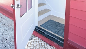 A red exterior door with a glass panel, a wooden staircase, and a doormat.