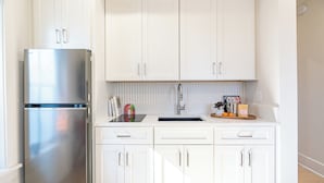 A kitchen with white cabinets, a stainless steel refrigerator, a sink, and a countertop with various items.