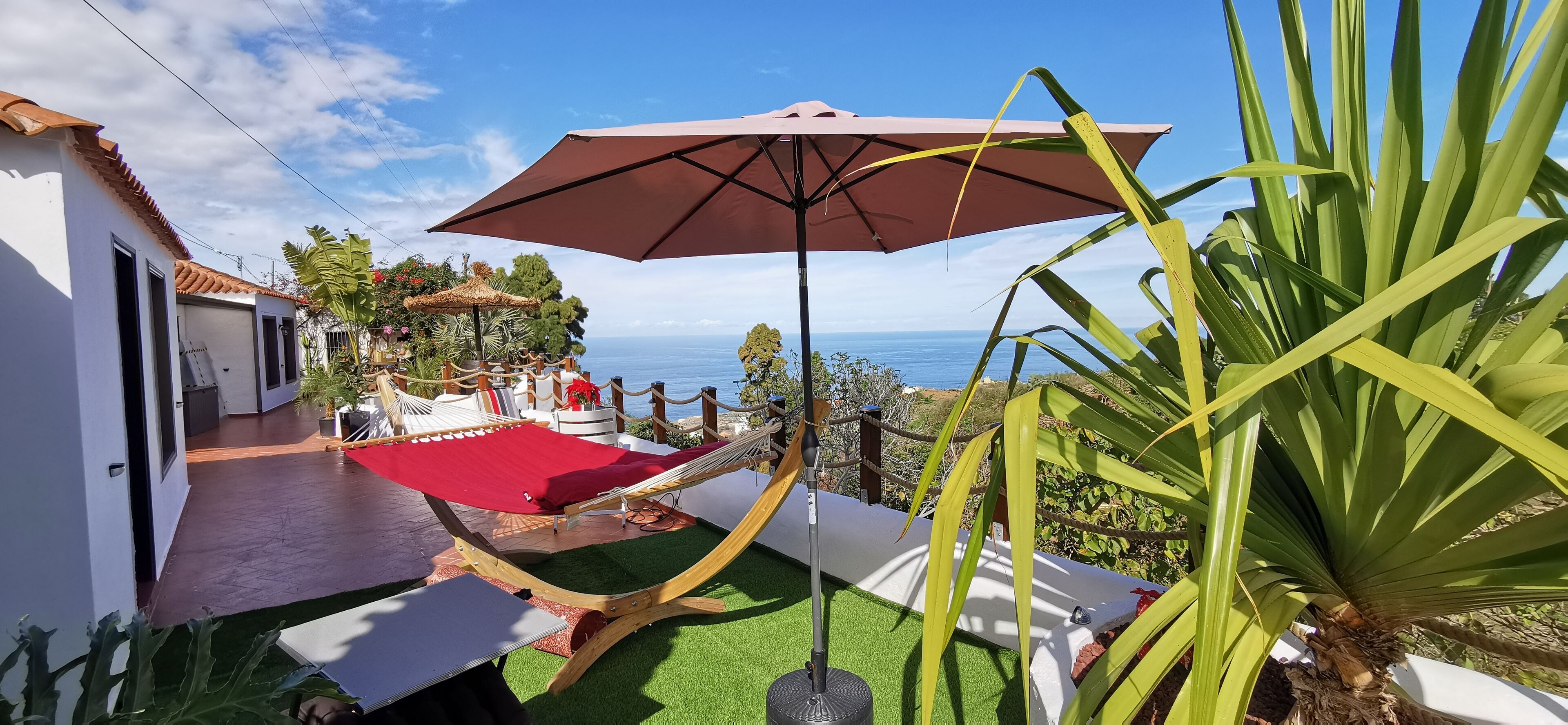 Un hamac sous un grand parasol, une moquette rouge et une vue sur la mer.