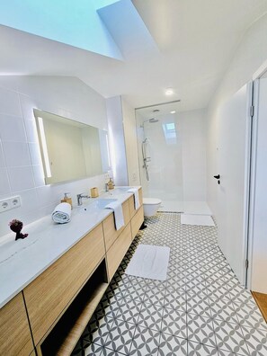 A modern bathroom with a large mirror, two sinks, a shower, and a patterned floor. - Spacious 3 bedroom large terrace&parking (Schuttrange)