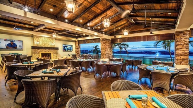 A restaurant with wicker furniture, a fireplace, and a view of the ocean. - Amazing Sunsets-Golf Country Club-Pickleball-Pools-Restaurant-Bar and more (Fort Myers)
