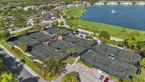 A large sports complex with multiple tennis courts, a parking area, and a lake in the background. - Amazing Sunsets-Golf Country Club-Pickleball-Pools-Restaurant-Bar and more (Fort Myers)