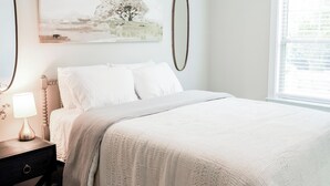 Un dormitorio con una cama, una mesita de noche, una lámpara, un ventilador de techo y una ventana.