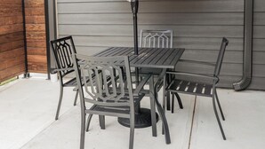 Un patio exterior con una mesa, sillas, un paraguas beige y una valla de madera.