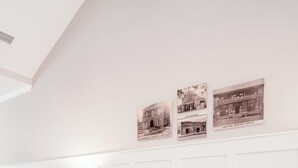 Una sala moderna con un sofá blanco, una mesa de centro de madera y una lámpara. Encima del sofá hay tres cuadros enmarcados en la pared.