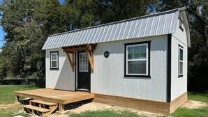 Une petite maison de plain-pied avec un toit en métal, un porche à l’avant et une terrasse en bois.