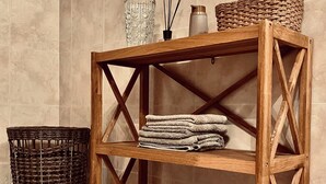 Une étagère en bois à trois niveaux, un sèche-cheveux noir, un panier tressé et un vase en verre avec un flacon à pompe.