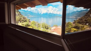 Une fenêtre donnant sur un lac, des montagnes et un village.