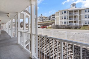 A covered walkway with white railings, leading to a building with multiple balconies and a stone retaining wall.