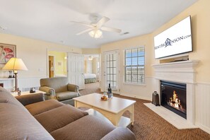 Een woonkamer met een open haard, een televisie en een plafondventilator.