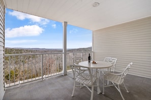 Un balcon abrité avec une table et des chaises, une bouteille et un verre.