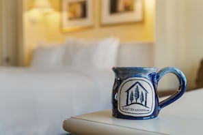 A ceramic mug with a logo on a table in a hotel room.