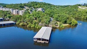 Una propiedad junto al lago con un muelle que se adentra en el agua, rodeada de abundante vegetación y edificios residenciales.