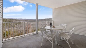 Ein Balkon mit rundem Tisch und weißen Stühlen, mit Blick auf eine hügelige Landschaft.