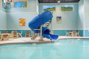 An indoor pool with a blue slide, lounge chairs, and artwork on the walls.