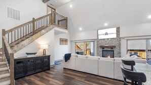 Un salón amplio con un sofá modular grande, una chimenea, una escalera de madera y un comedor con mesa y sillas.
