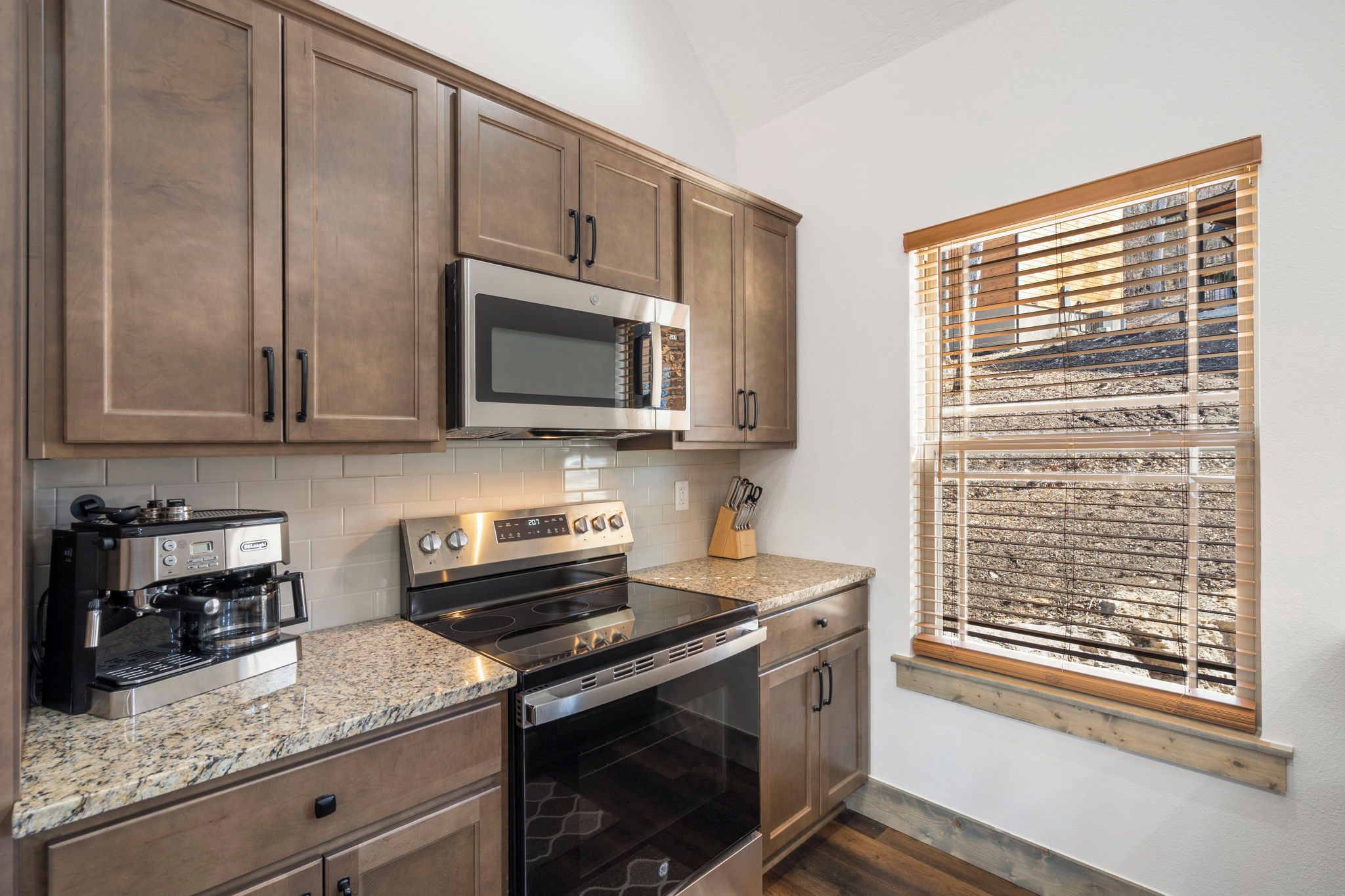 A kitchen with wooden cabinets, a microwave, a stove, and a window with blinds.