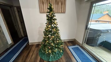 A Christmas tree with lights and ornaments in a room with wooden flooring and a window.