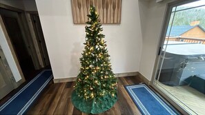 Ein mit Lichtern und Schmuck verziertes Weihnachtsbaum in einem Zimmer mit Holzboden und einem Fenster.