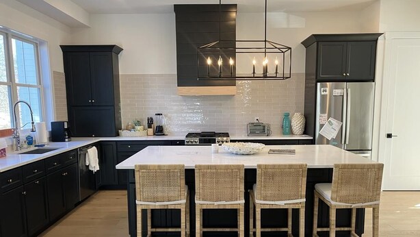 Una cocina moderna con una isla grande, muebles oscuros y una lámpara colgante.