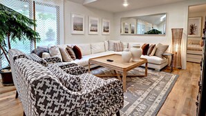 A modern living room with a sectional sofa, patterned armchairs, a coffee table, and a large mirror. - Charming Lakefront Home~Hot Tub~Fire Pit~Large Covered Deck (Fayetteville)