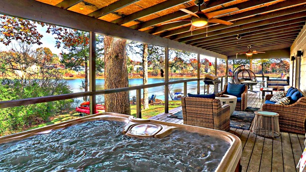 A hot tub area with a view of a lake, wicker furniture, and a ceiling fan. - Charming Lakefront Home~Hot Tub~Fire Pit~Large Covered Deck (Fayetteville)