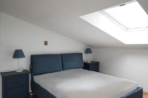 A bedroom with a skylight, a bed, two bedside tables with lamps, and a small decorative item on the wall.