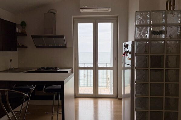 A kitchen with a large island, a double door leading to a balcony, and a refrigerator with a glass door.