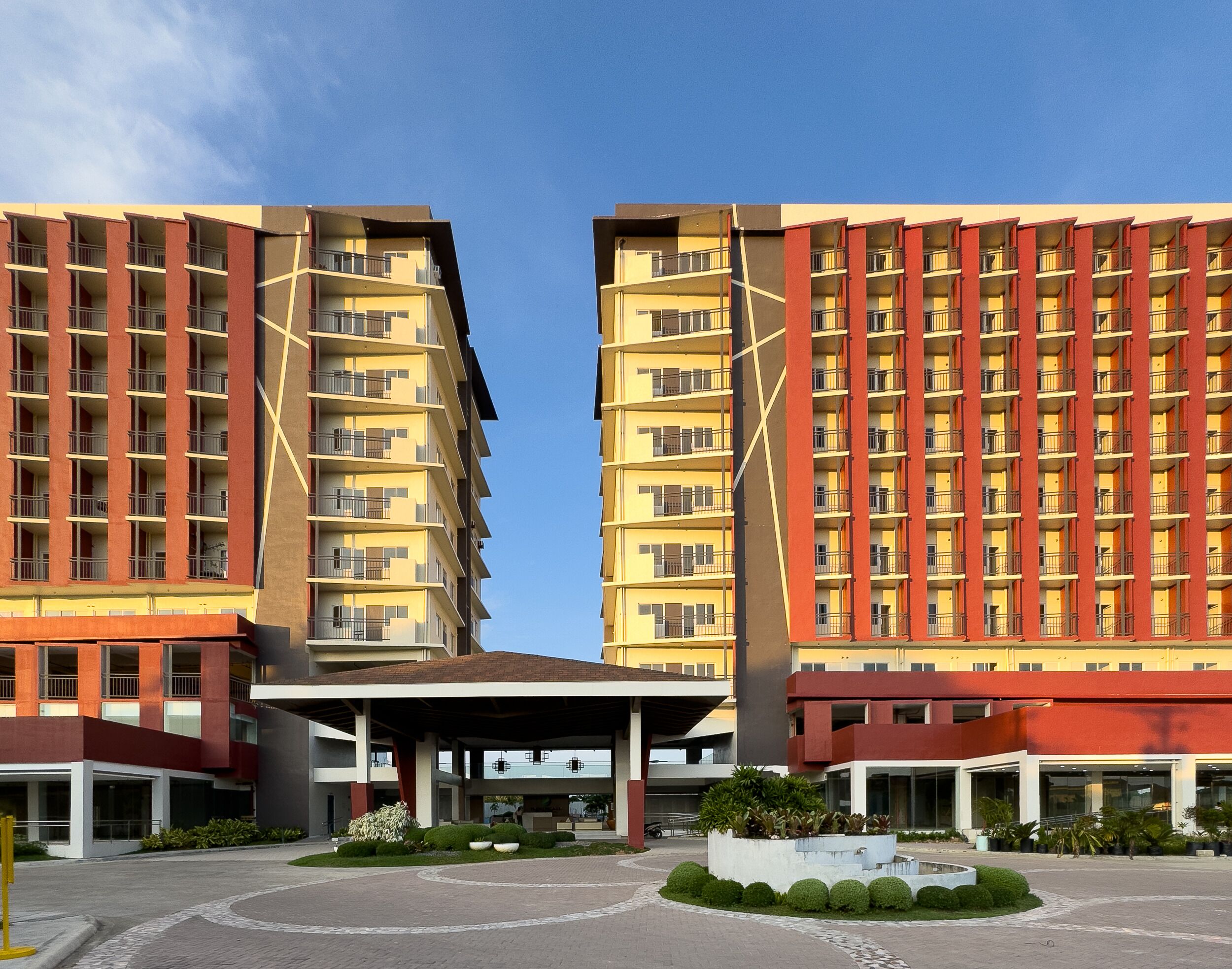 A modern hotel with a symmetrical facade, multiple balconies, and a central entrance area with a covered walkway.