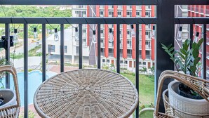 En balkon med fletmøbler, udsigt til en rød bygning og hængende lyskæder.