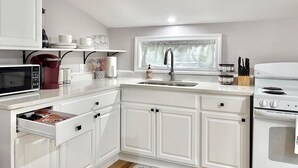 Une cuisine avec des meubles blancs, un four à micro-ondes, une machine à café, un évier et une cuisinière.