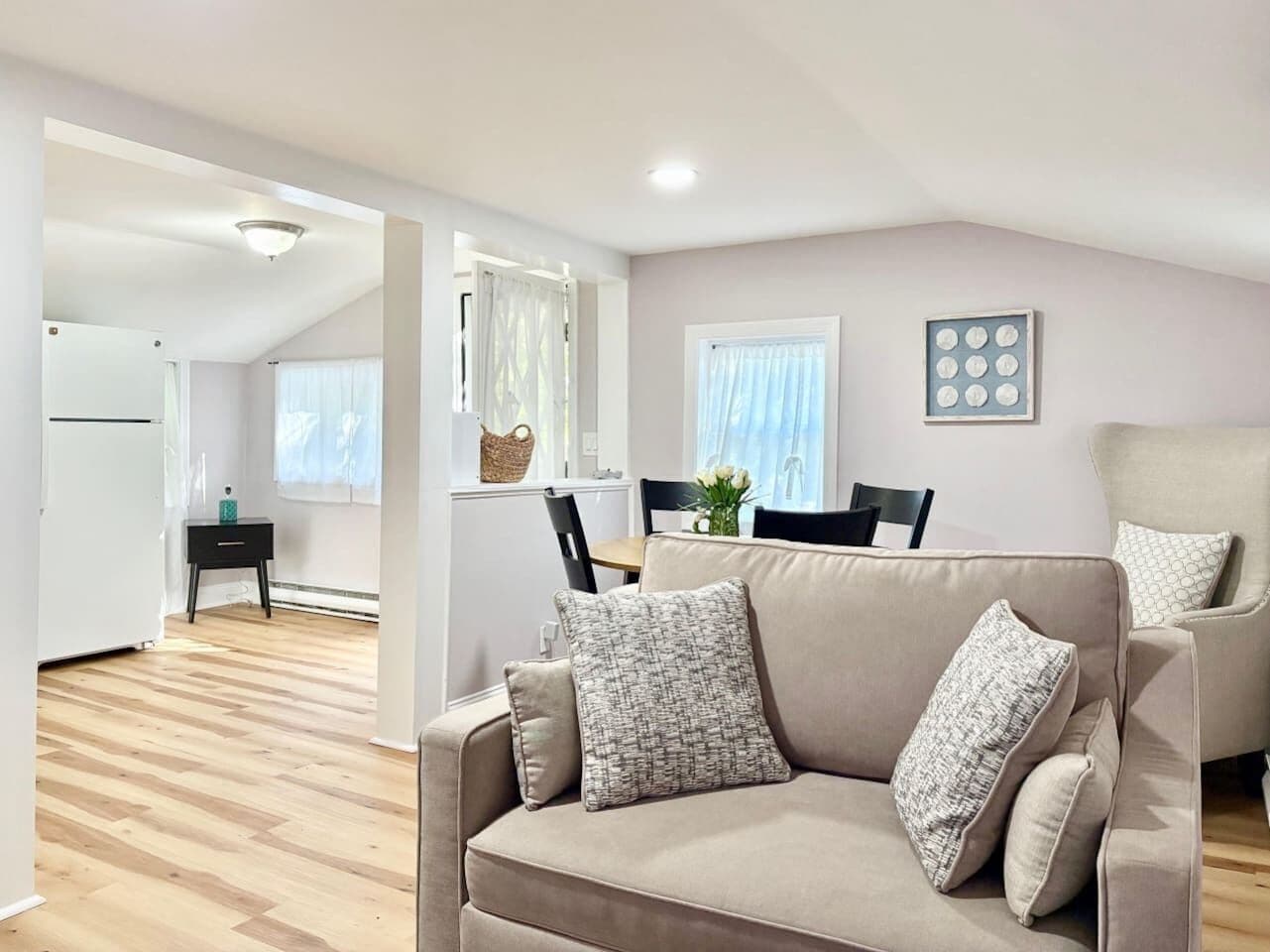 Een moderne woonkamer met een beige bank, een eettafel met stoelen, een keukenhoek en een plafondlamp.