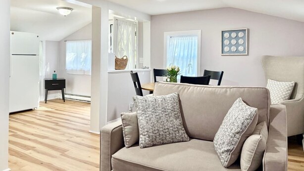 Un salon moderne avec un canapé beige, une table à manger avec des chaises, un coin cuisine et un luminaire au plafond.