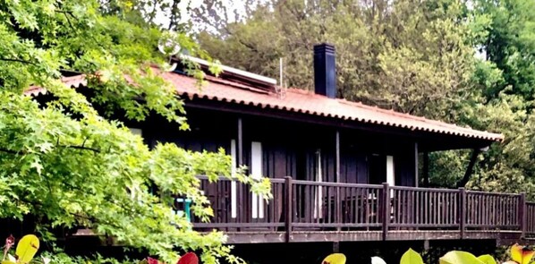 A wooden cabin with a balcony, surrounded by lush greenery.