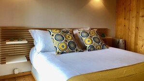 Una cama bien tendida con almohadas estampadas, una mesita de noche con lámpara y un cabecero de madera.