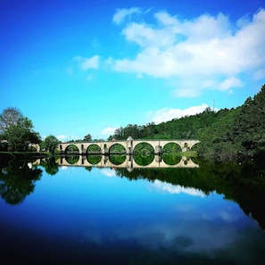 A bridge with multiple arches over a calm body of water, surrounded by lush greenery and a clear blue sky. - Villa With Pool in Arcos de Valdevez (Arcos de Valdevez)