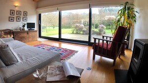 A spacious living room with a large sliding glass door leading to a garden, a cozy sofa, a red armchair, and a fireplace.