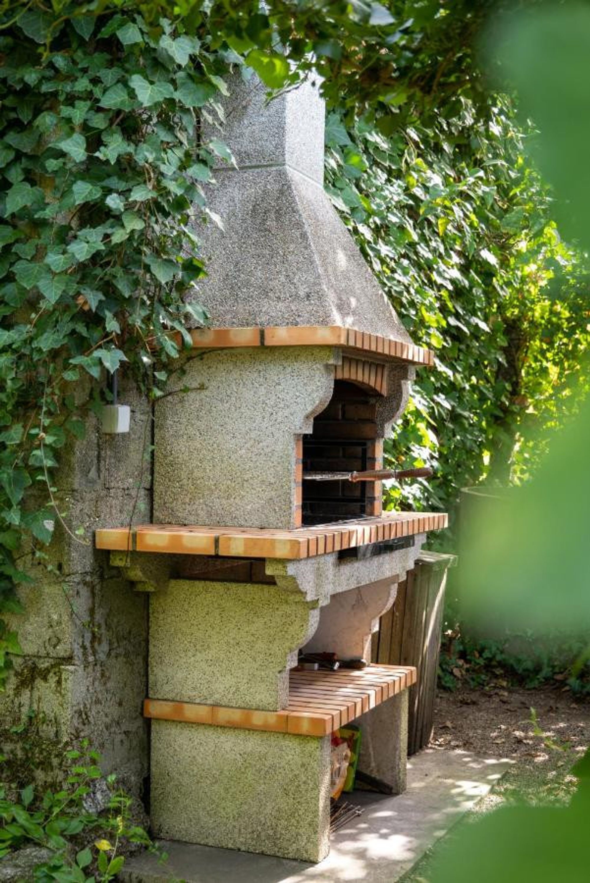 Estructura exterior de piedra con chimenea, rodeada de vegetación.